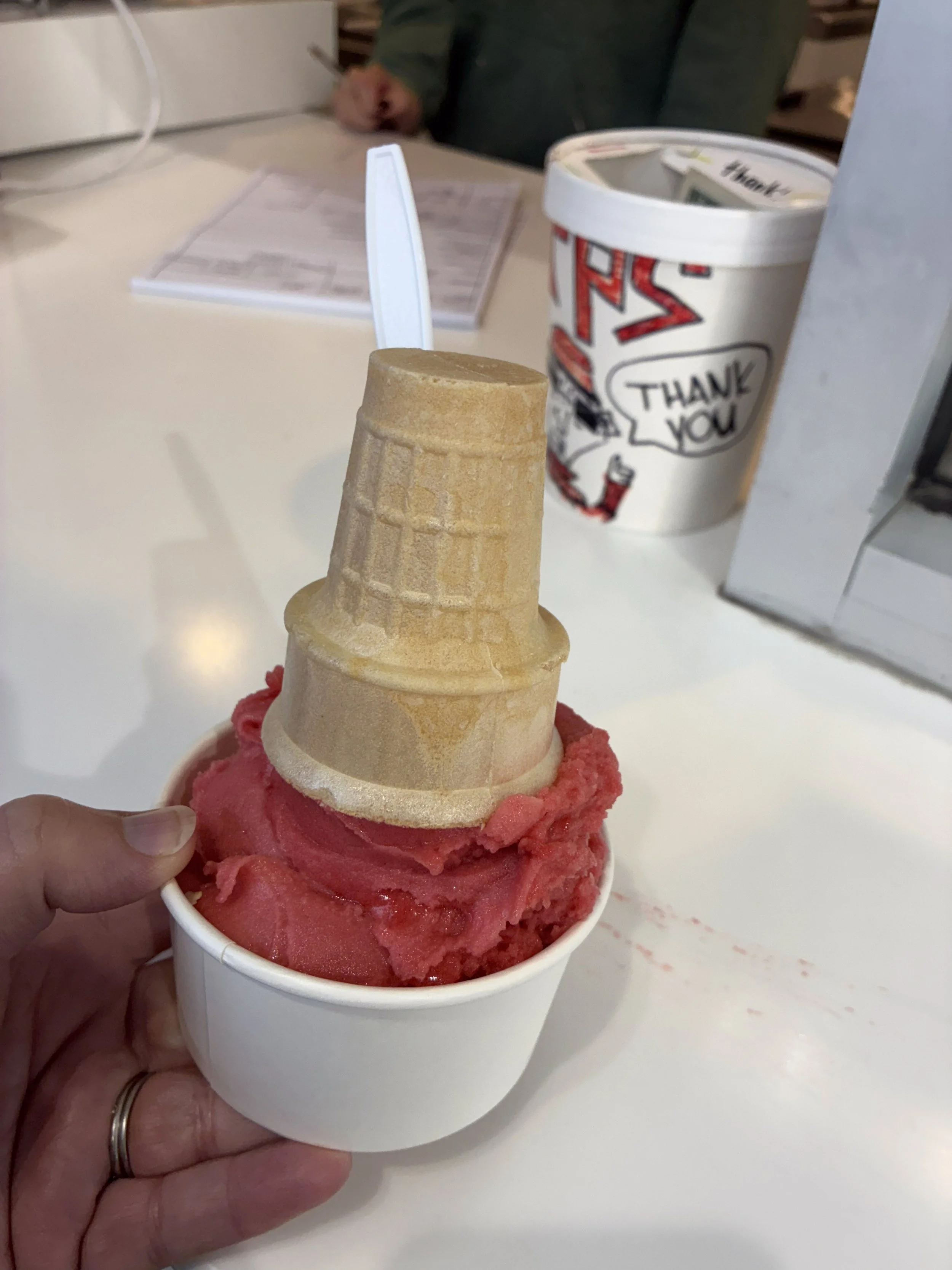 A cup of raspberry ice cream with an upside-down cone on top.