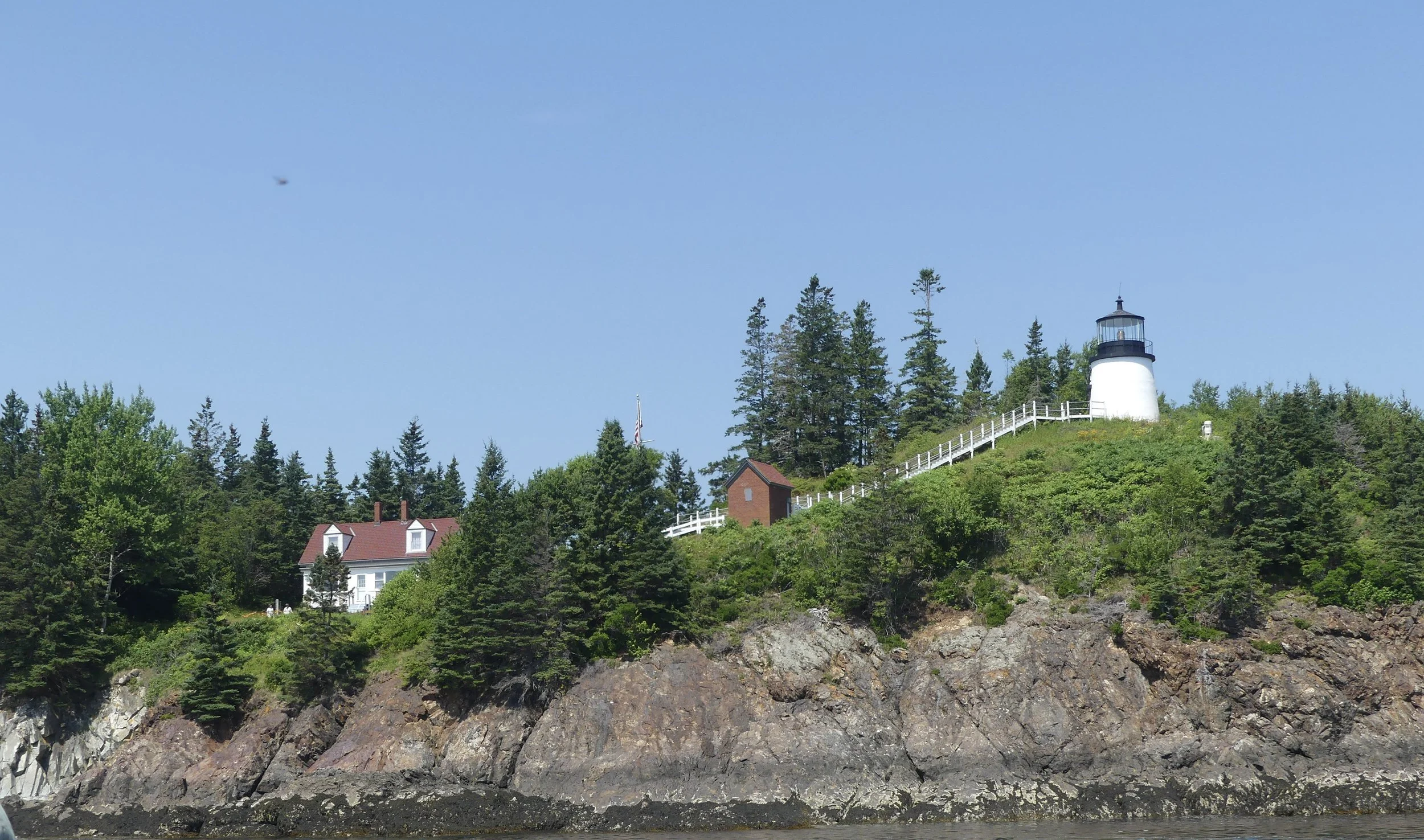 A lighthouse on a wooded, rocky headland.