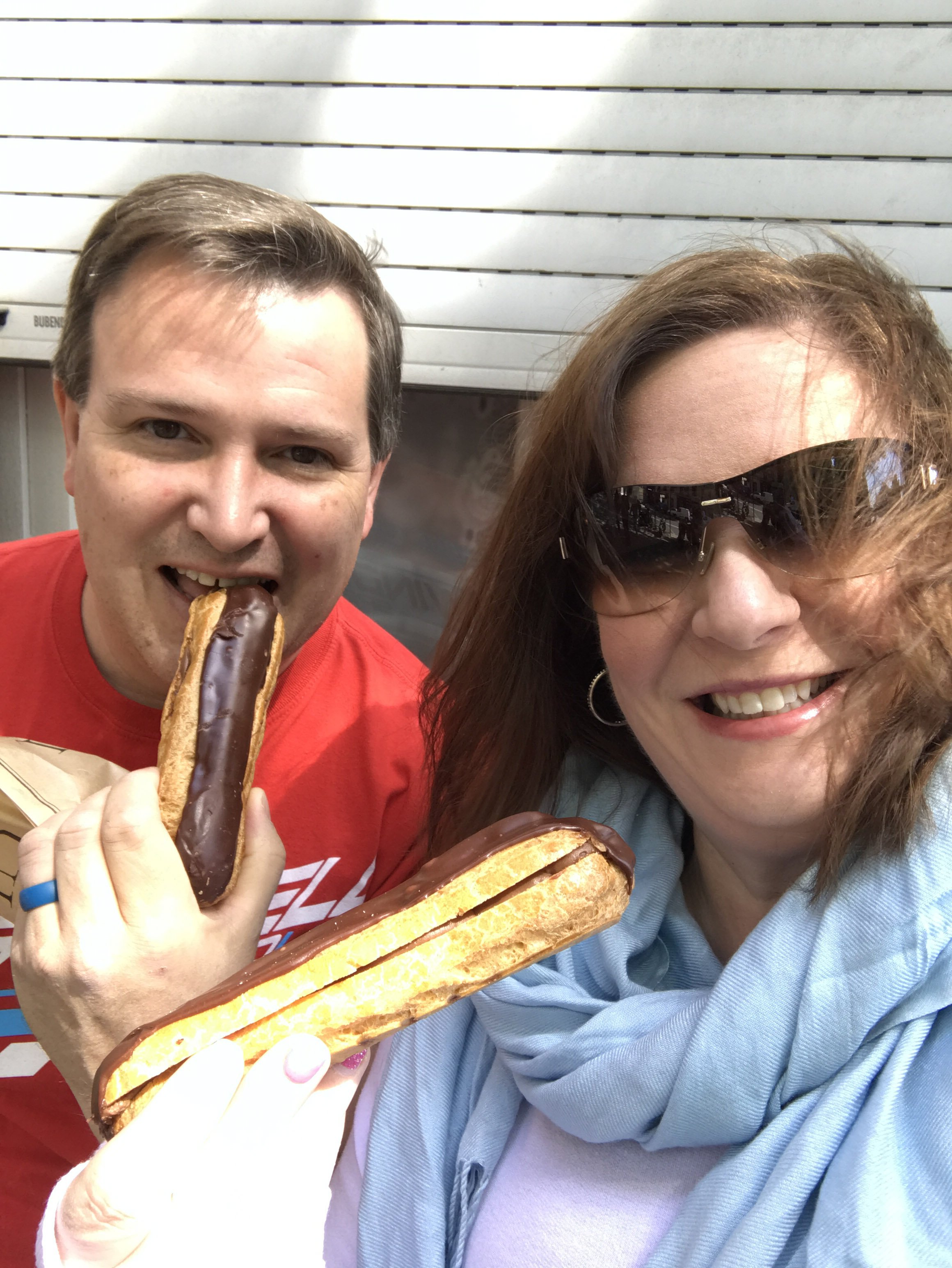 A couple holding éclairs for a selfie.