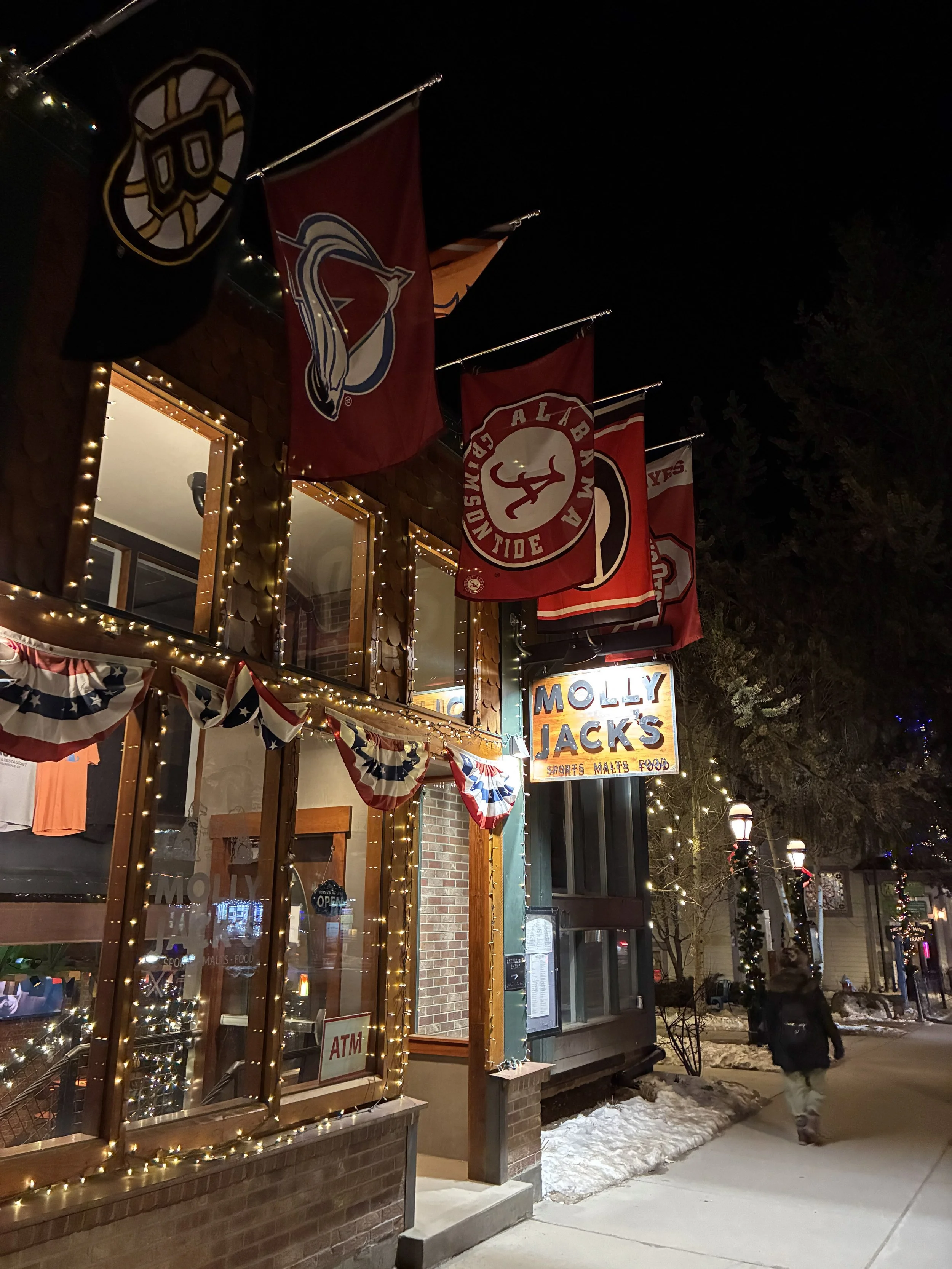 Sports flags and string lights outside Molly Jack's at night.