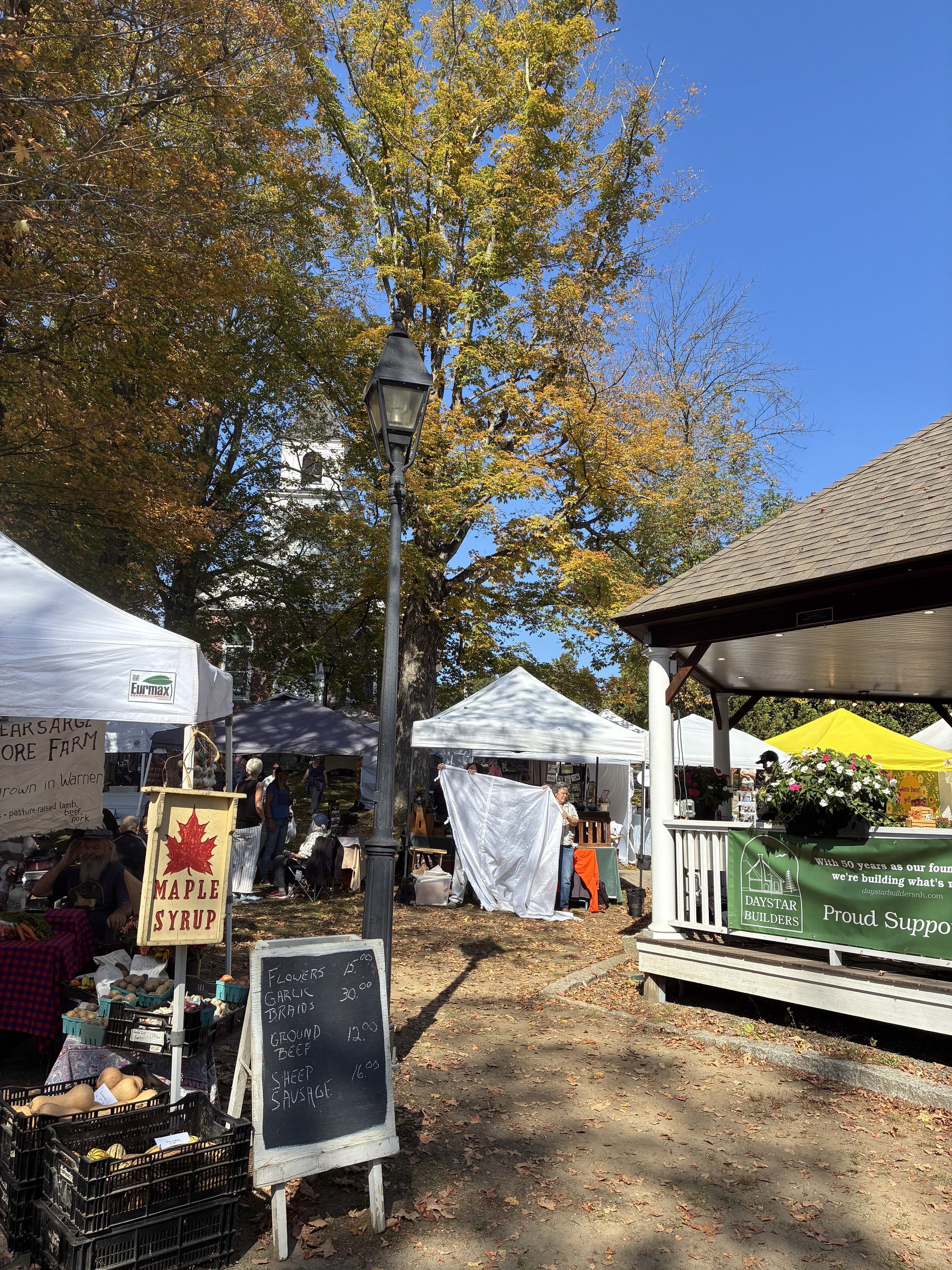An outdoor farmers market with a maple syrup stand and a gazebo.