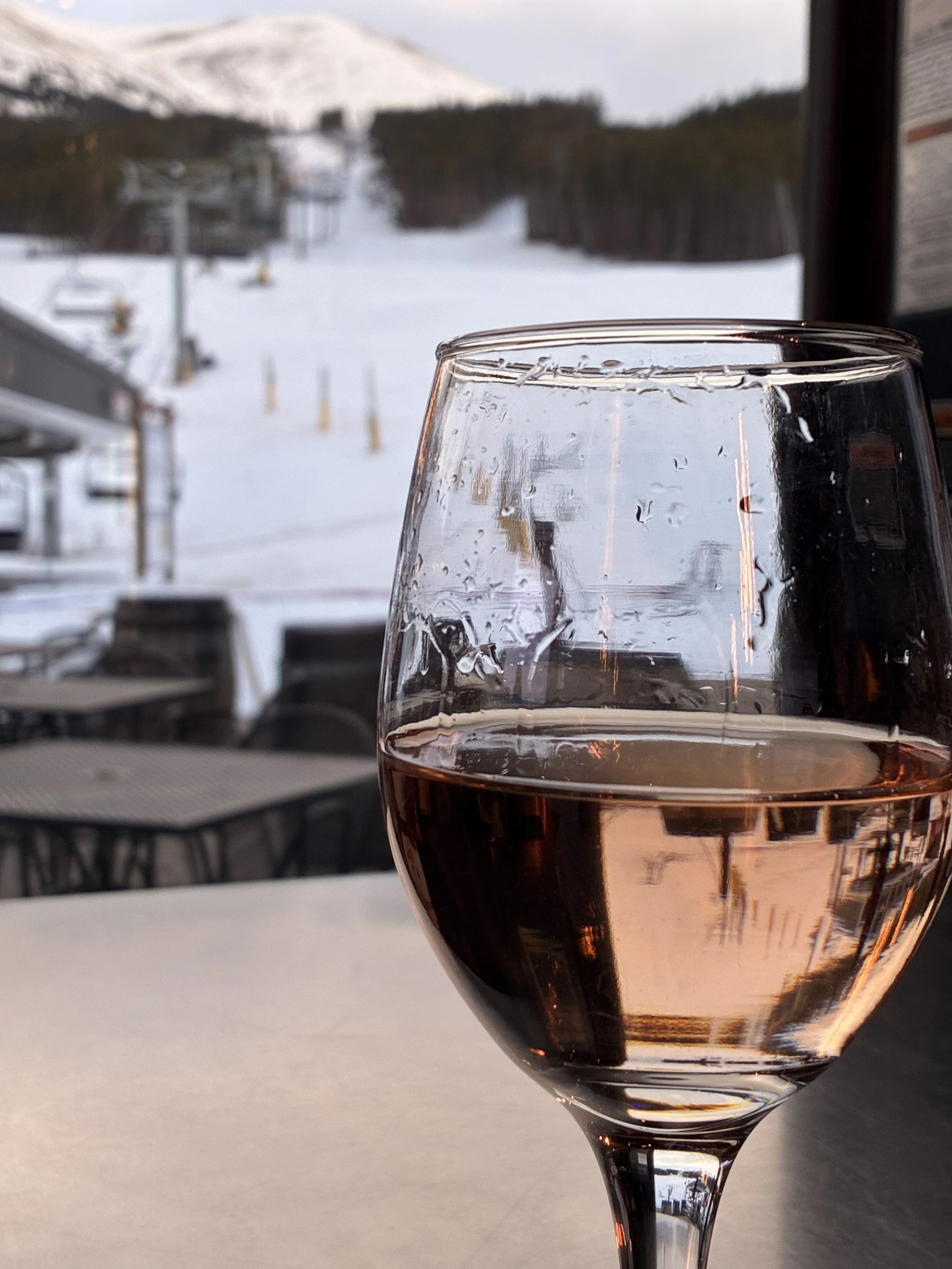 A glass of wine with snowy slopes and a chairlift in the background.