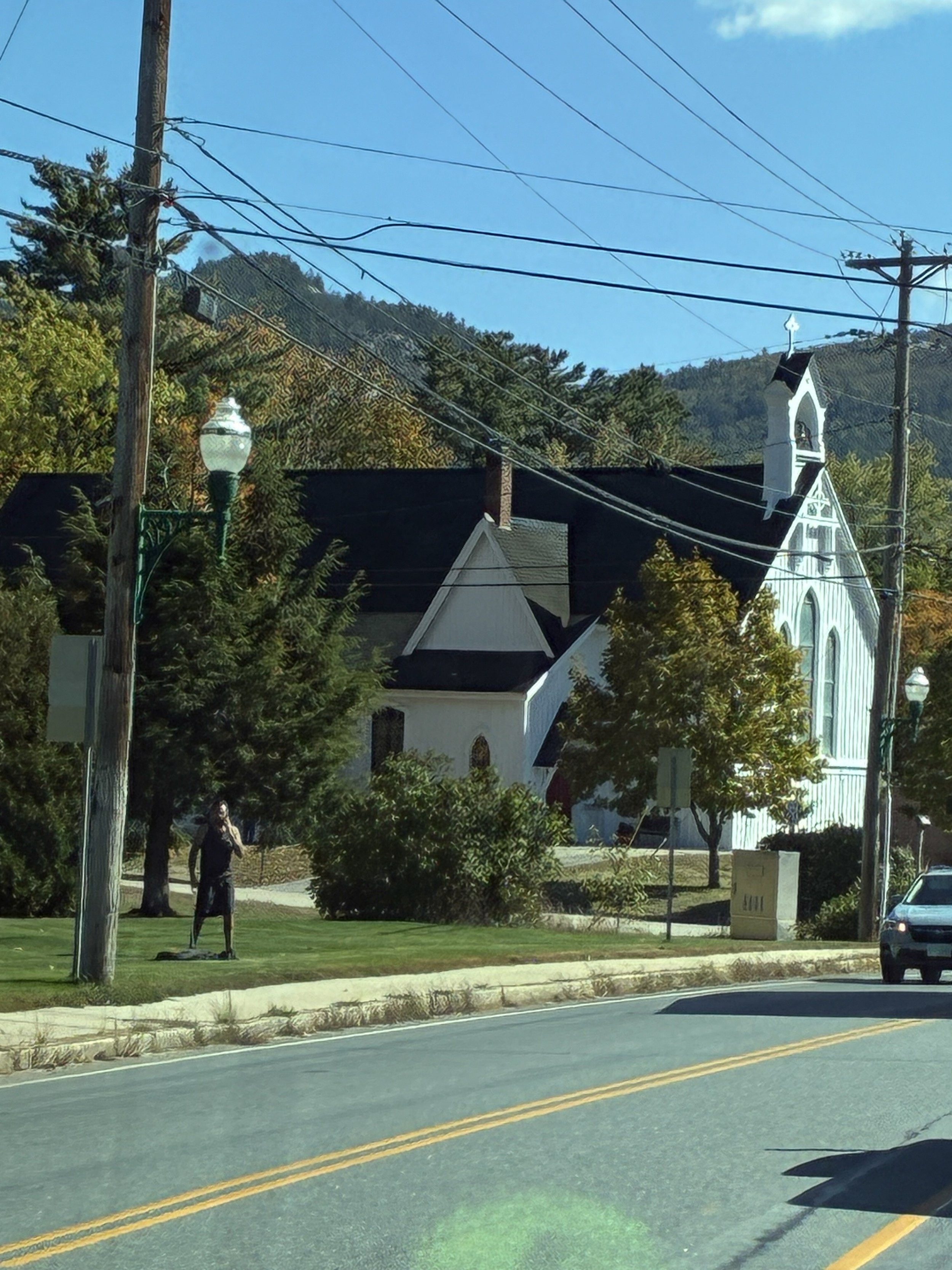 A white church on a New England town street with fall-color mountains behind.