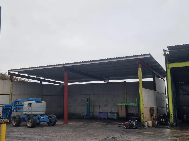 Steel columns and roof beams being assembled beside an existing industrial building