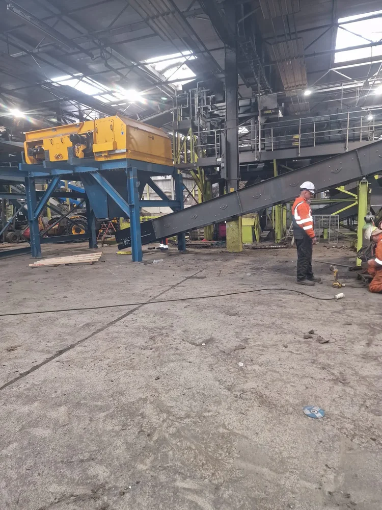 Processing equipment connected to an inclined conveyor, with workers alongside during installation