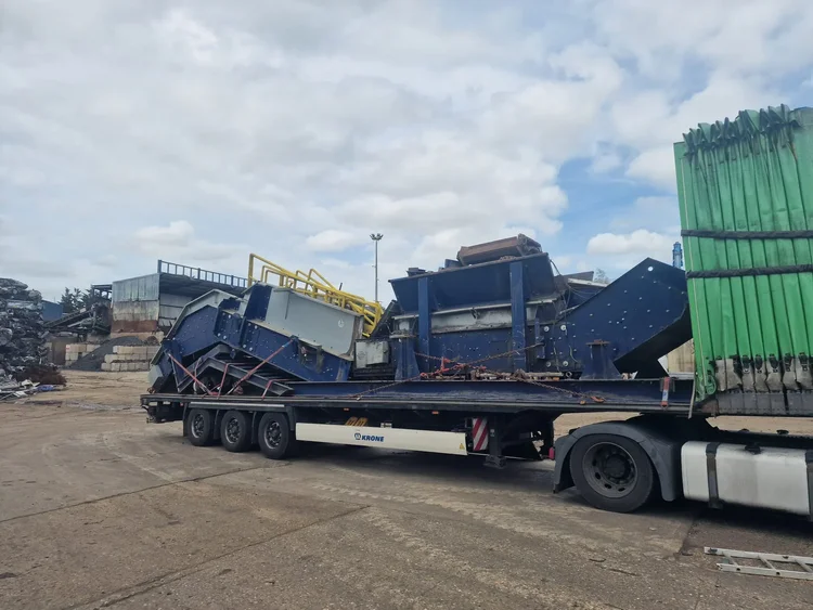 Disassembled blue processing equipment secured on a flatbed trailer at an industrial site