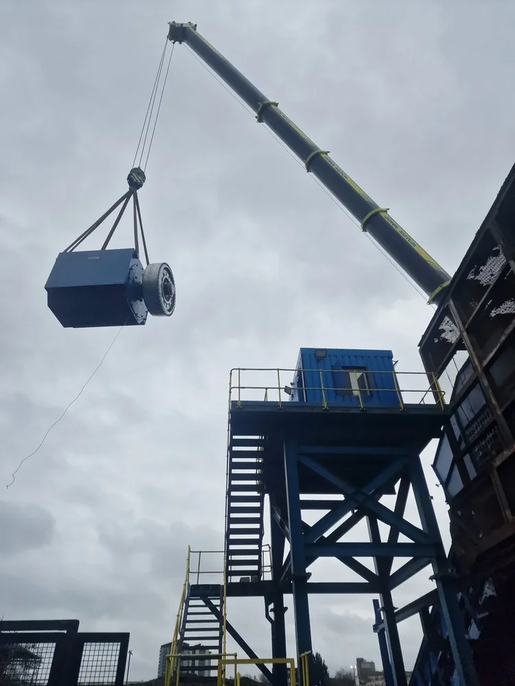 A crane lifting a blue industrial machine beside a raised steel access platform