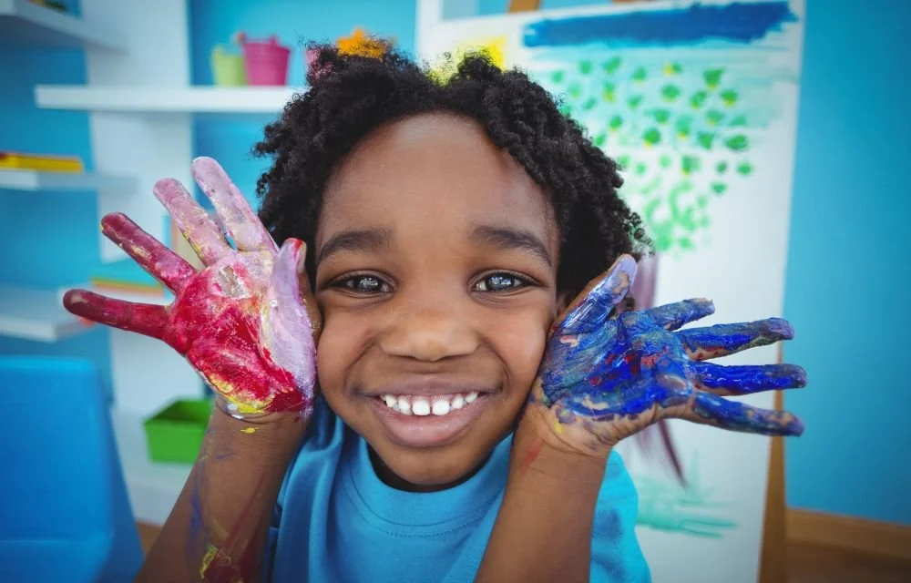 A happy young camper smiling with paint on both hands at Surpass summer camp