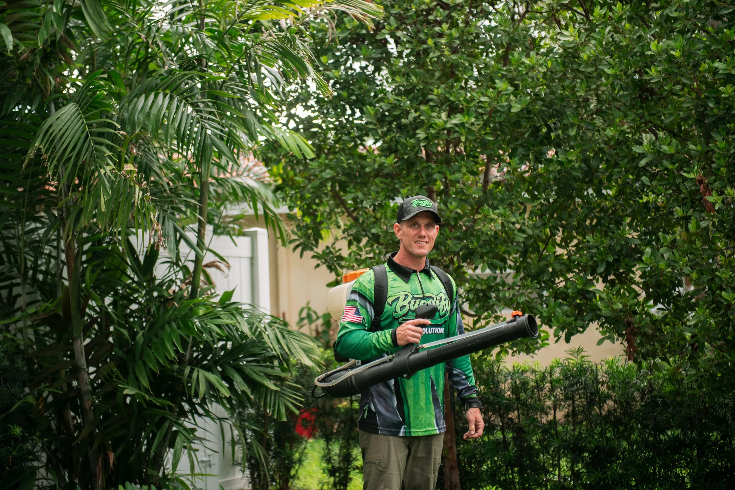 Buggify technician smiling with a mist-blower in garden greenery, shown faintly behind the FAQ