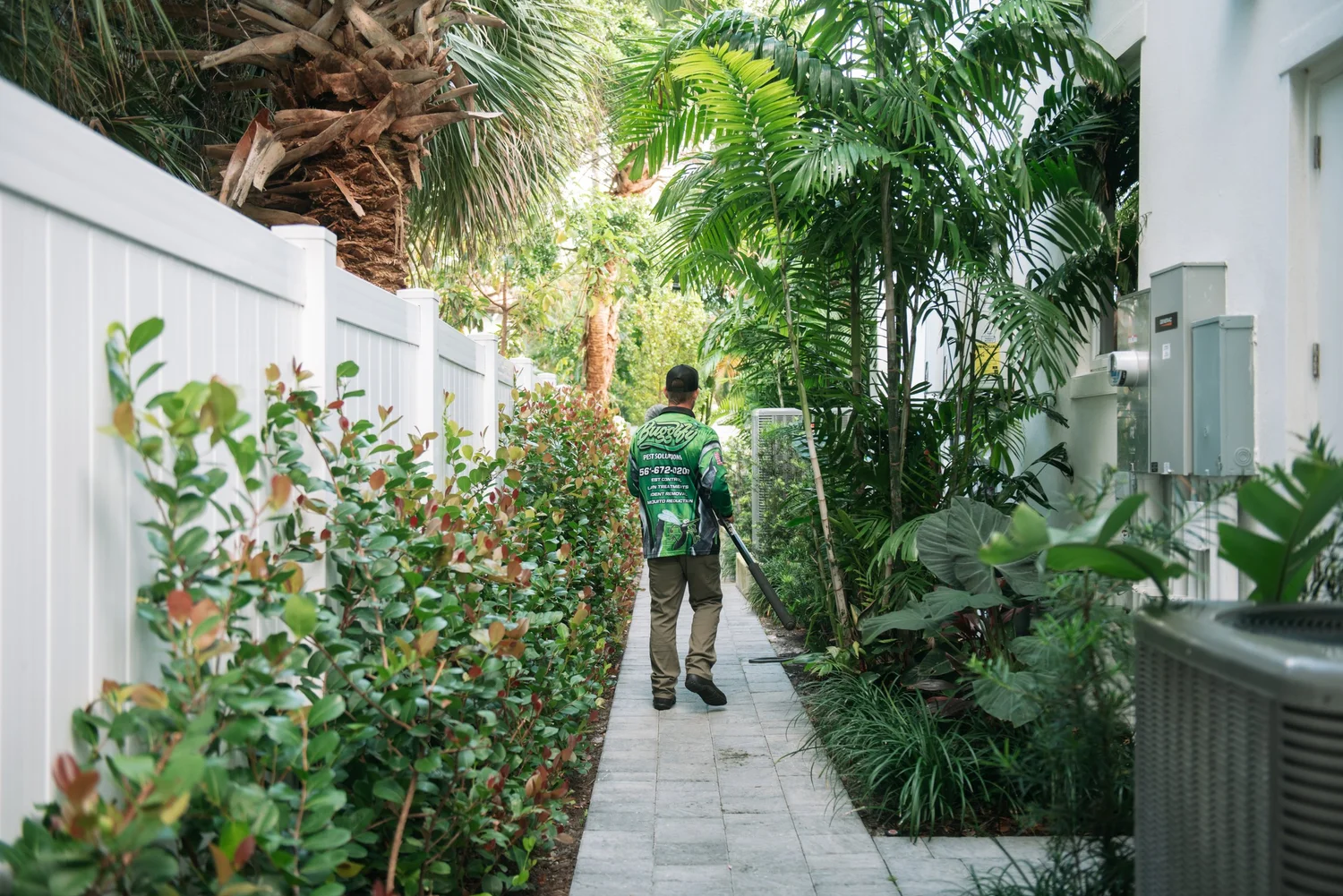 Buggify technician walking a narrow side-yard path between a fence and lush plants during a property inspection