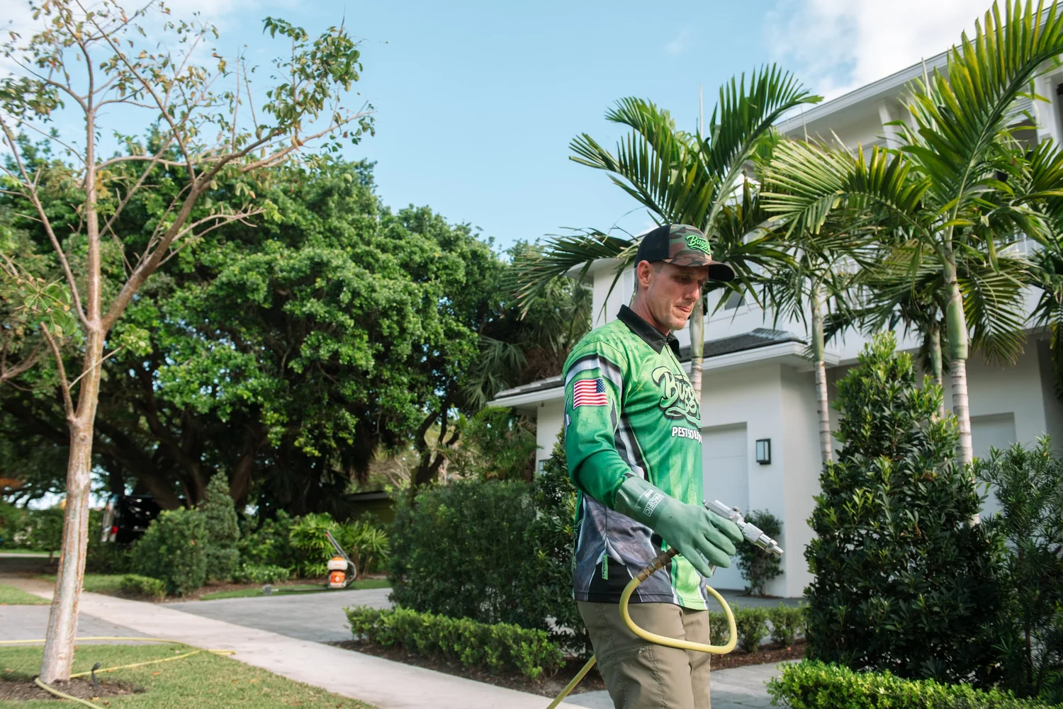 Buggify technician with a spray wand in a side yard with palms and white homes behind