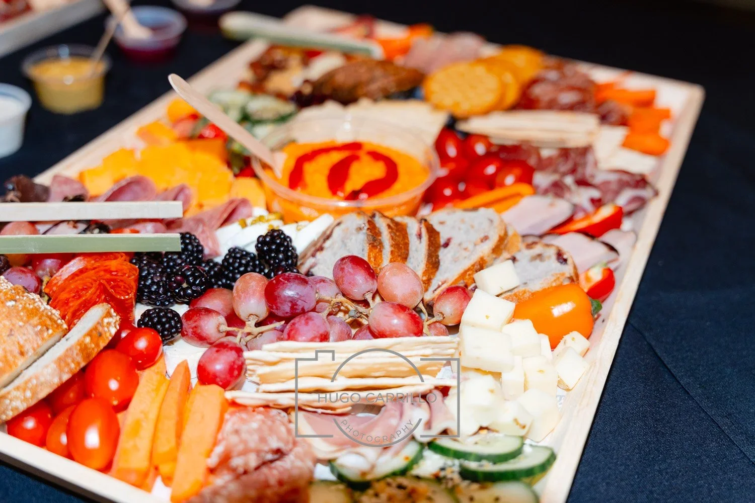 Charcuterie board with assorted meats, cheeses, grapes, blackberries, cherry tomatoes, sliced vegetables, and condiments.
