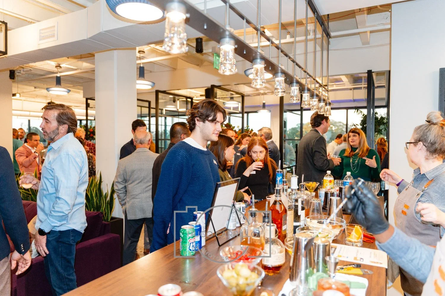 People socializing at a bar or event space with drinks and snacks on a counter.