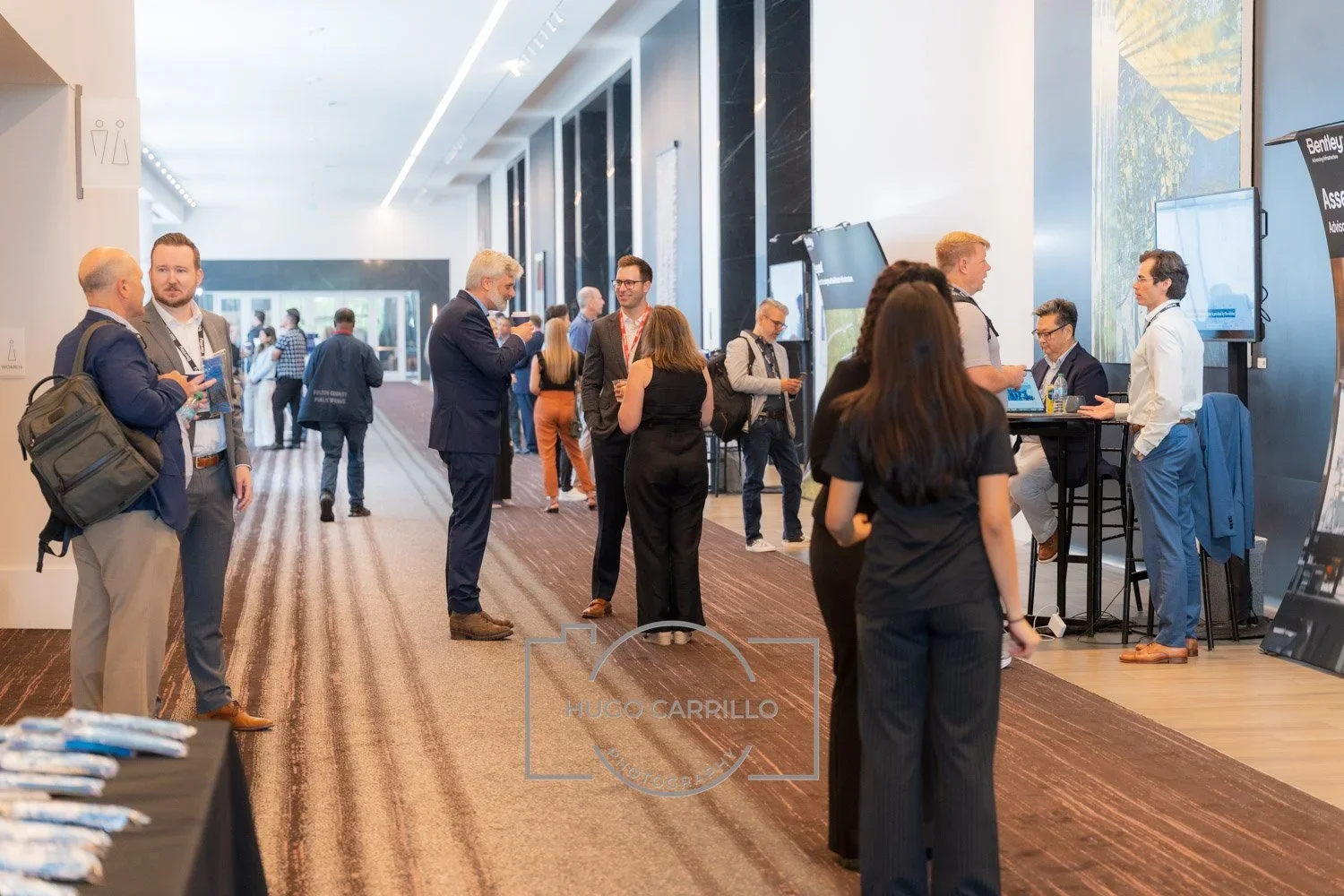 People mingling and talking at a professional networking event or conference in a spacious, well-lit corridor.