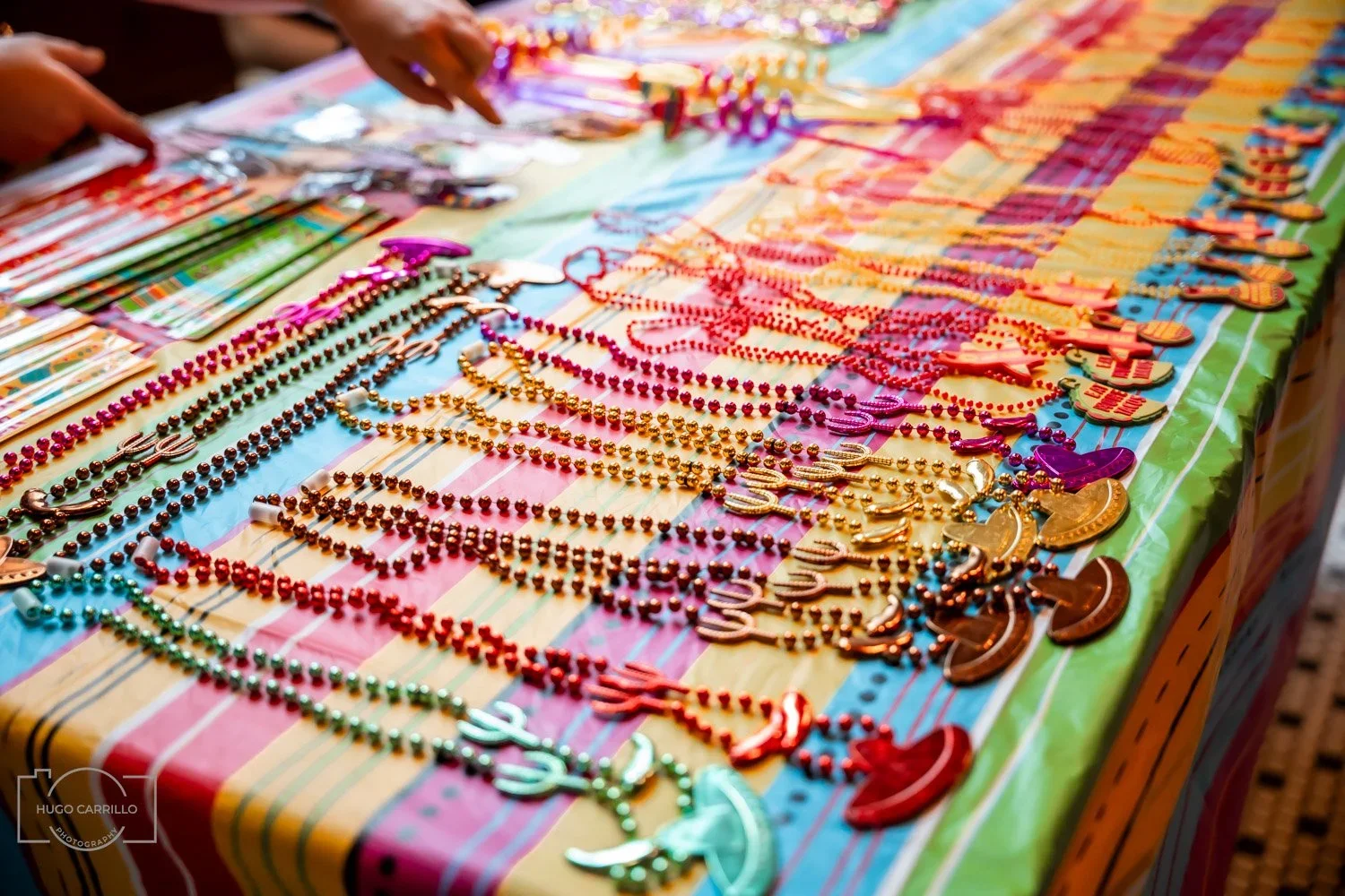Colorful display of jewelry including necklaces and bracelets on a checkered tablecloth, with hands reaching out to select items.