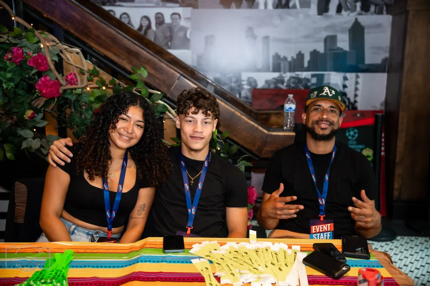 Three event staff members sitting at a table with colorful tablecloth, smiling and posing for the camera.