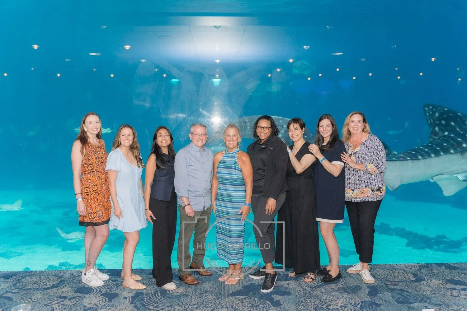 Group of nine people standing in front of an aquarium with a whale shark in the background.