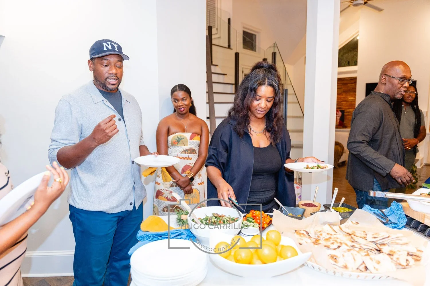 People serving themselves food at a buffet table during a social gathering in a home.