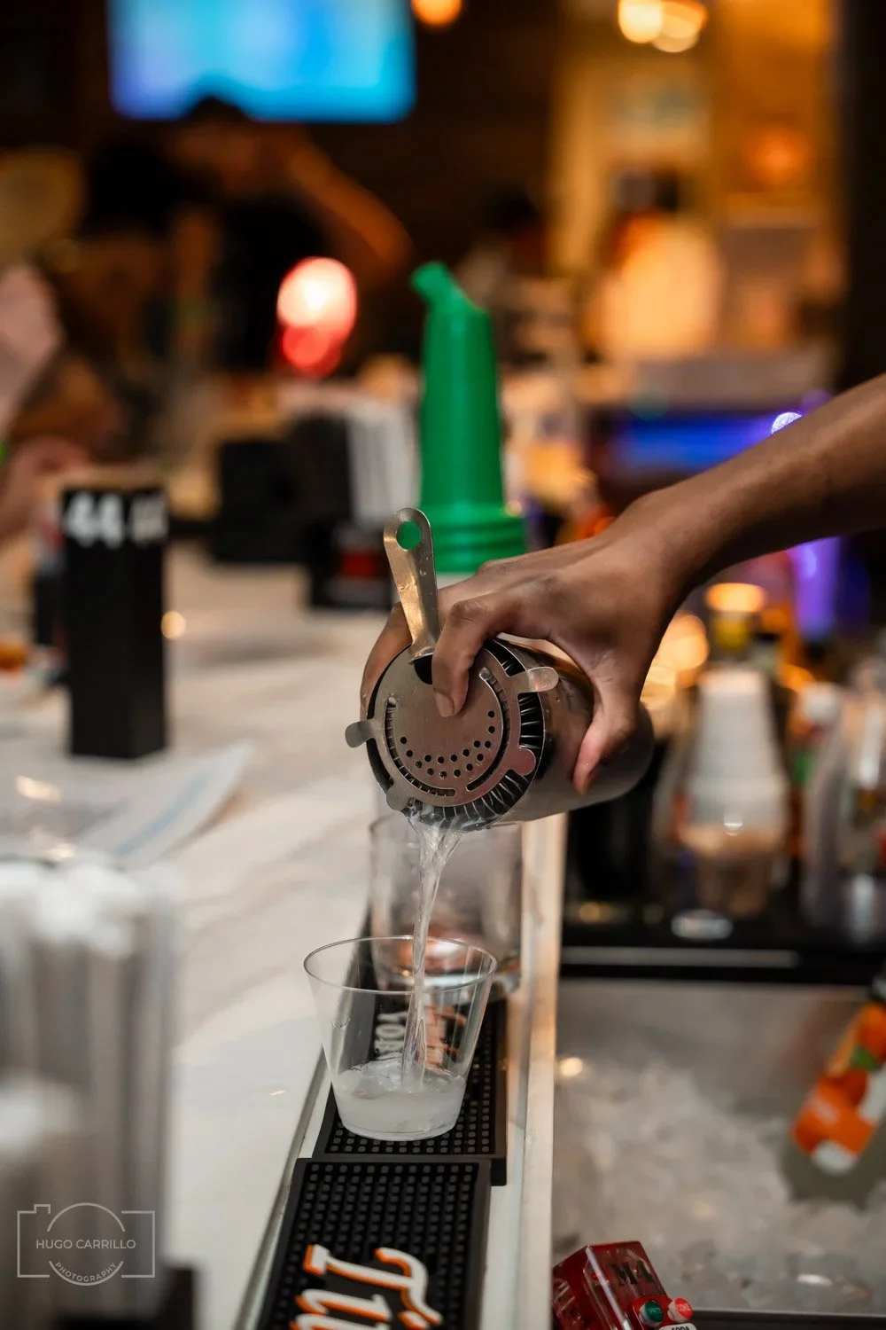 A person pouring a clear liquid through a cocktail strainer into a glass at a bar counter.