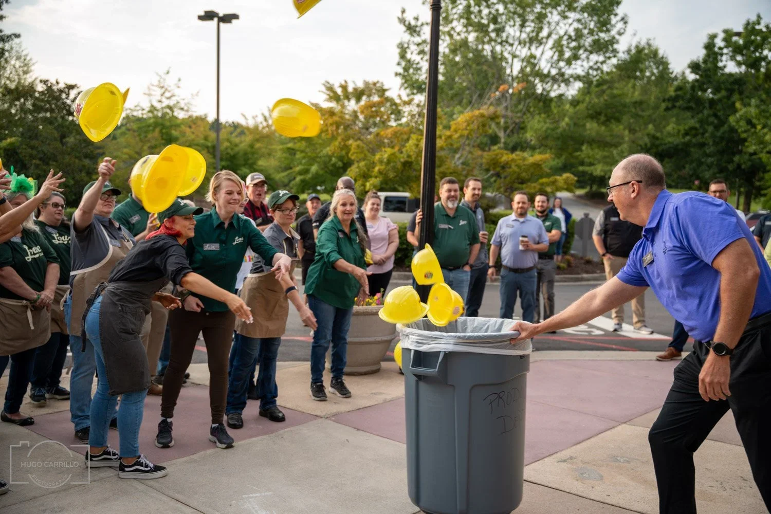 People throwing yellow construction hats into a trash can during a gathering outside.