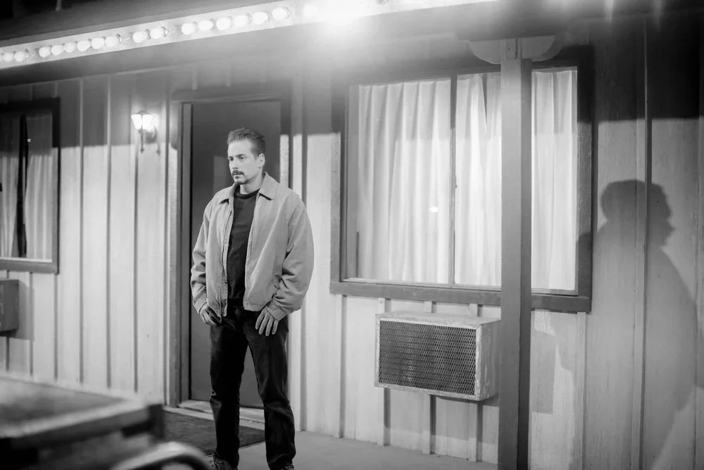 Actor outside a motel room beneath the marquee lights