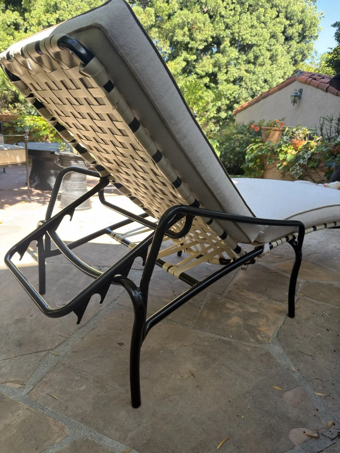 Back view of a chaise lounge showing woven strap support beneath its fitted cushion