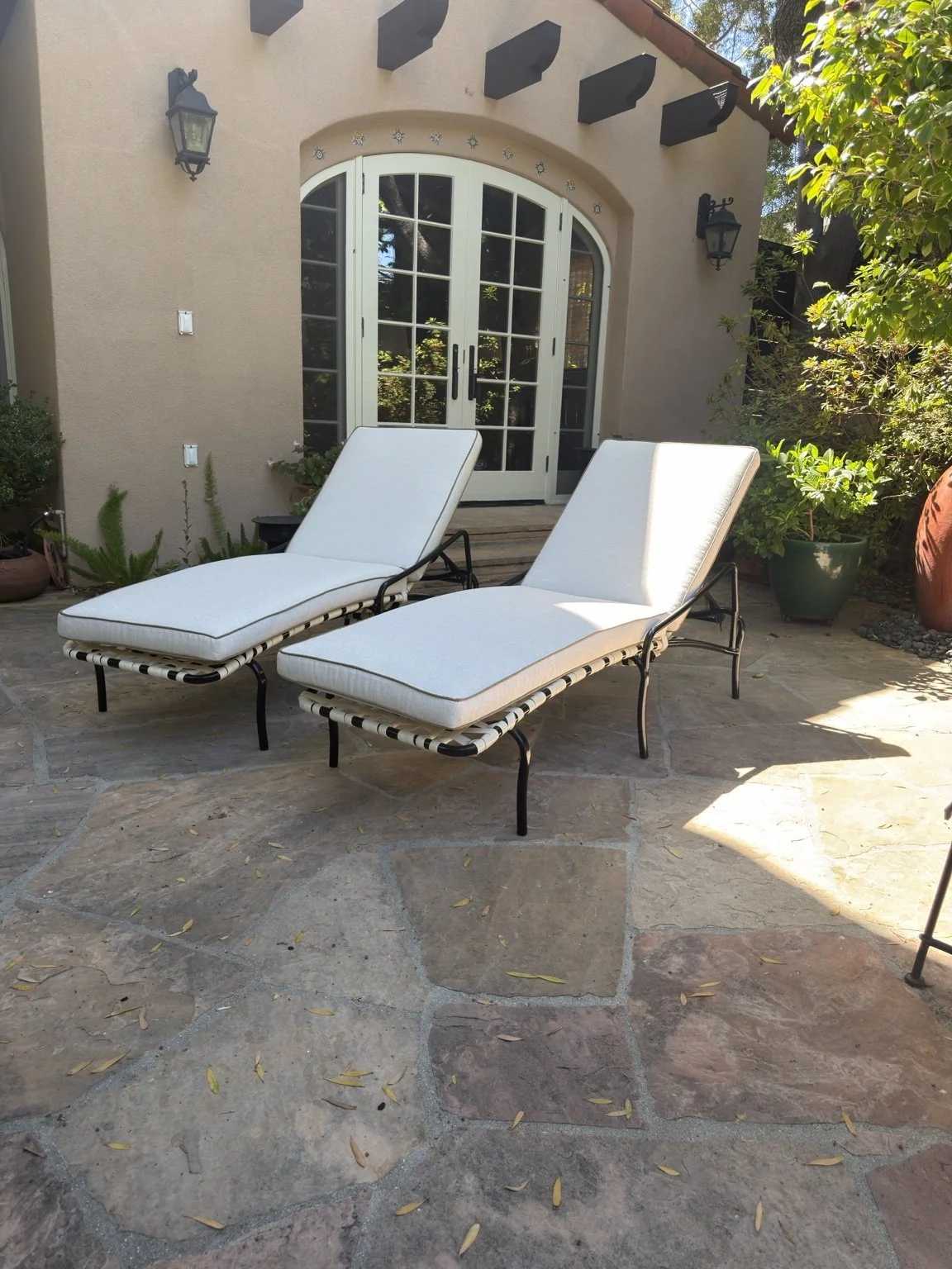 Two black metal chaise lounges with fitted pale seat and back cushions on a stone patio