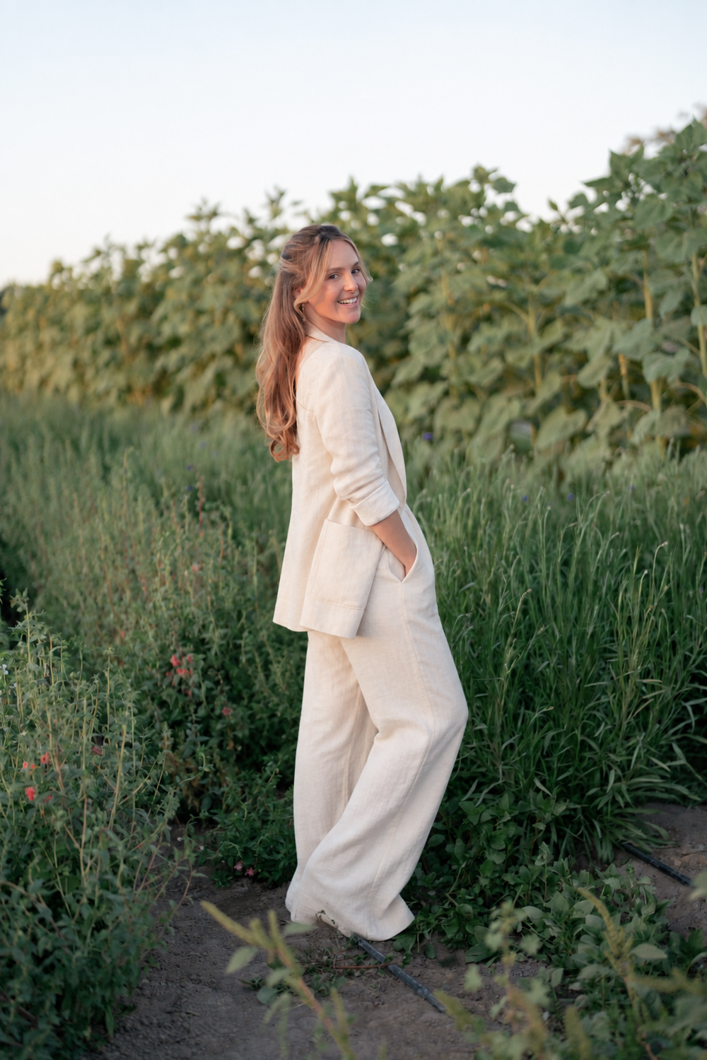 Emily Dubbe in a cream linen suit, smiling in a field of sunflowers