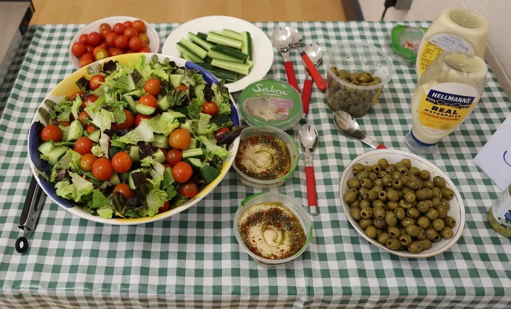 A table laid for the free community meal at The Table on a Tuesday — salad, bread and dishes set out on a chequered cloth