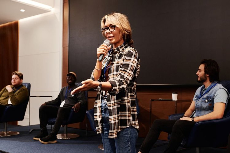 A woman speaking into a microphone before a seated audience.