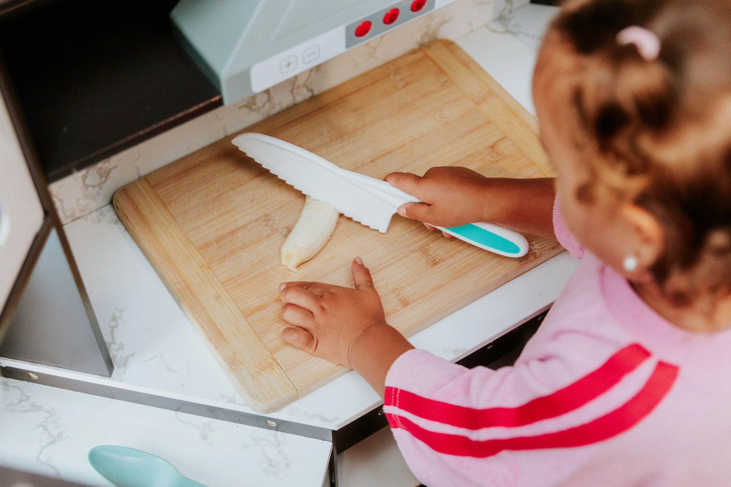 Little hands slicing banana on a wooden board