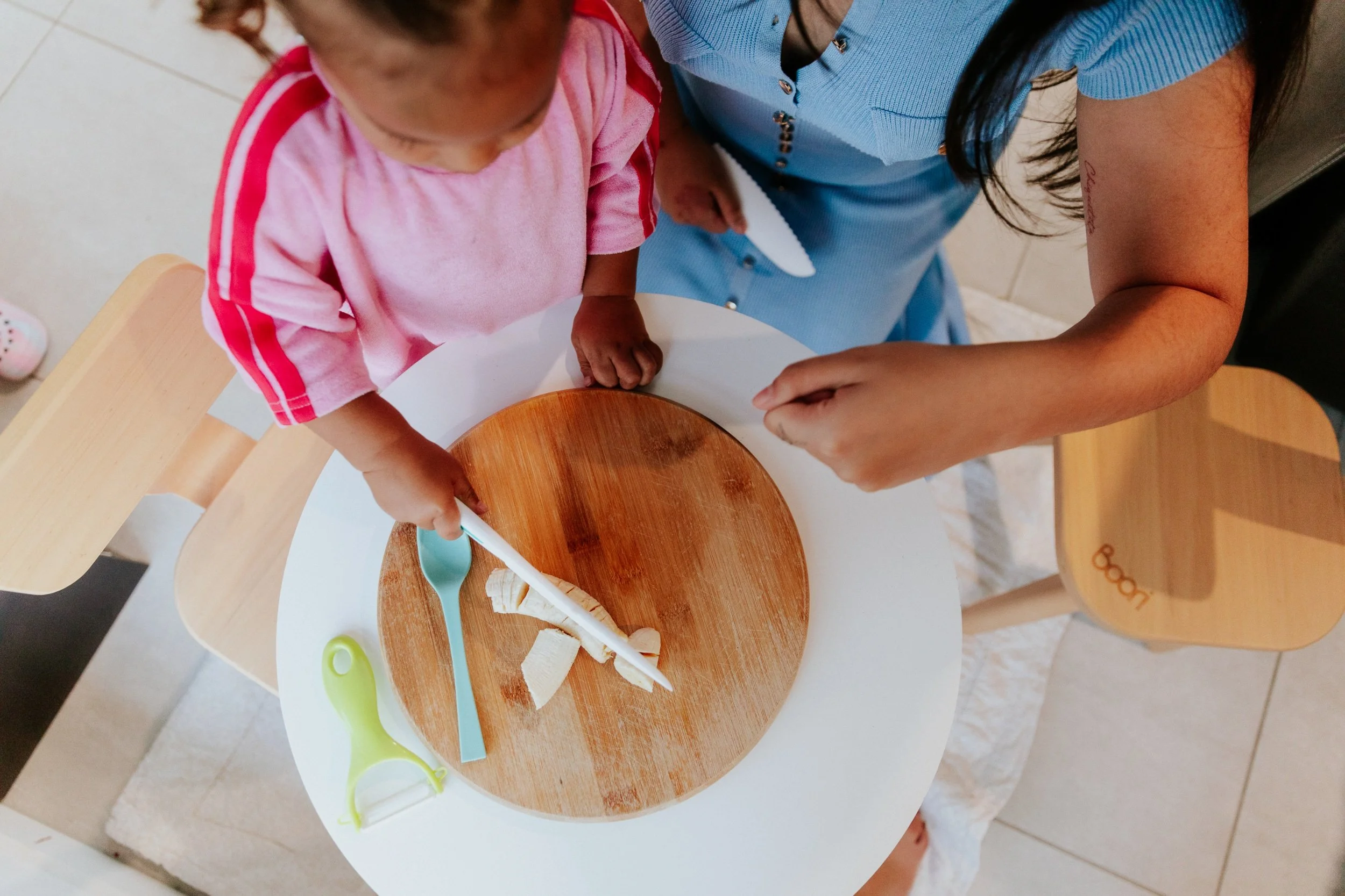 A parent and little one preparing food together at a small round table