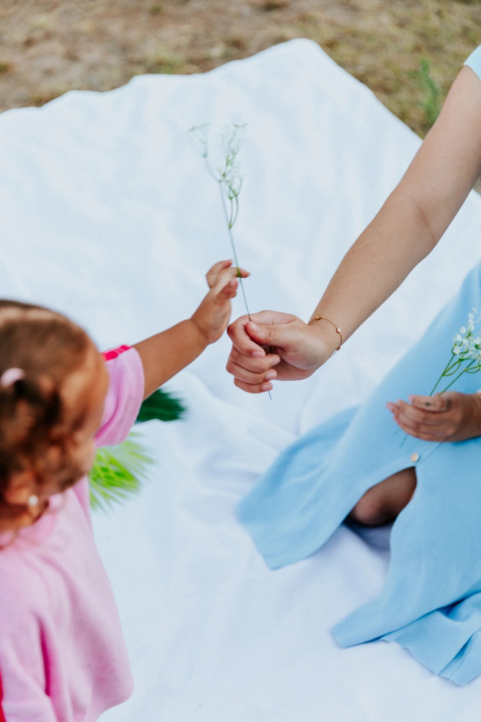 A child and parent sharing a small posy of wildflowers on a picnic blanket