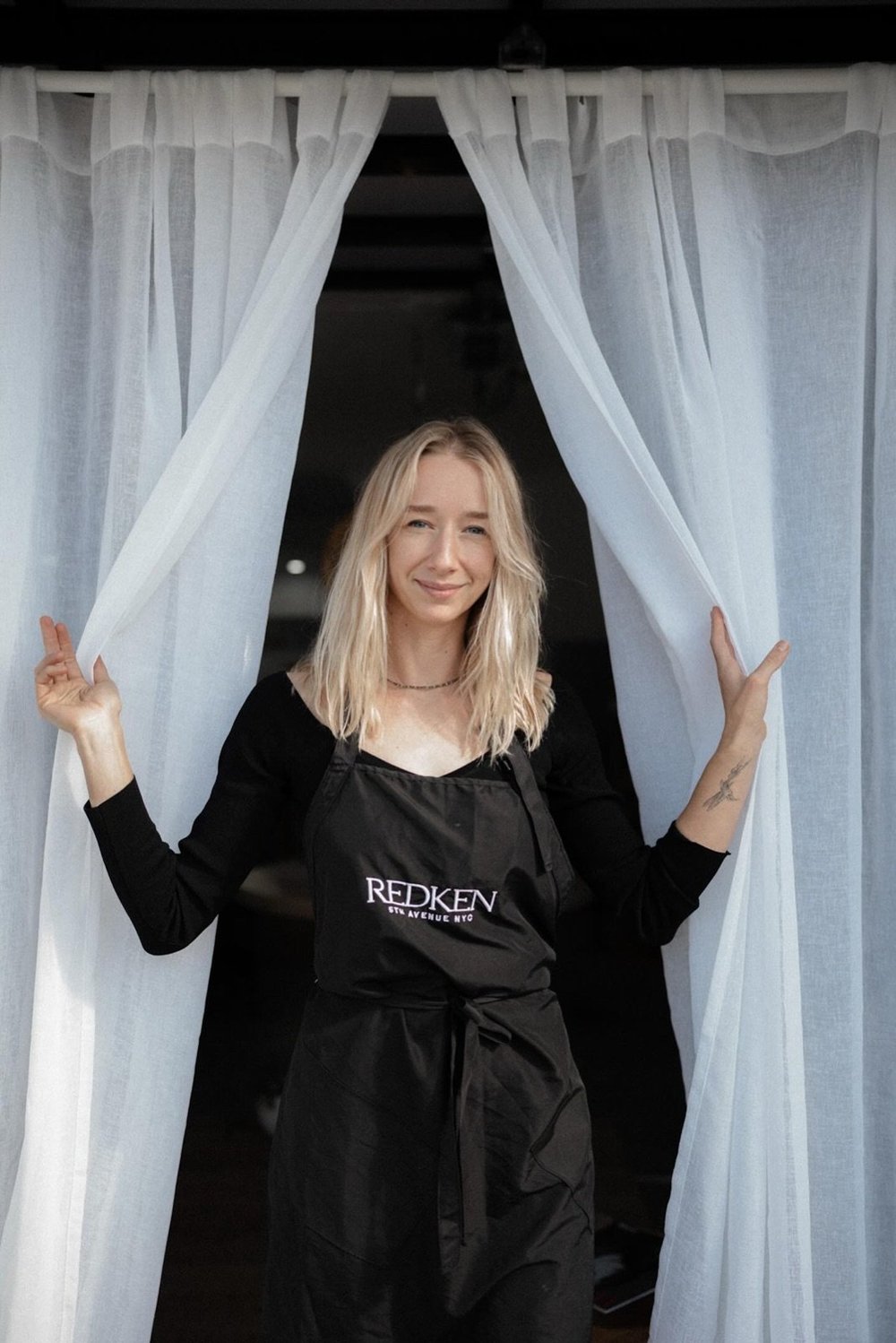 Kateryna at the studio entrance, between the white curtains