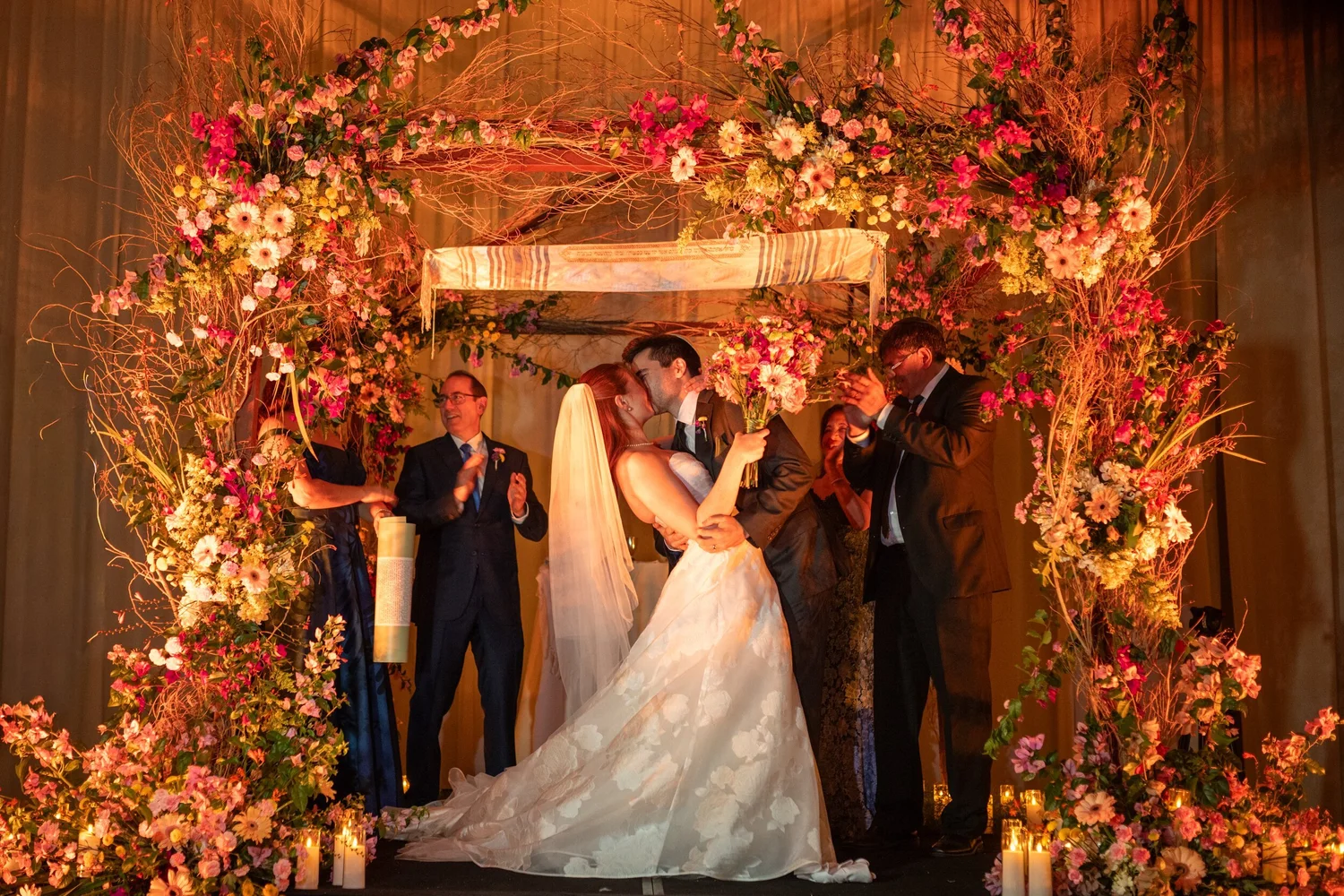 Sharon y Josh se besan bajo la jupá de flores rosadas y naranjas