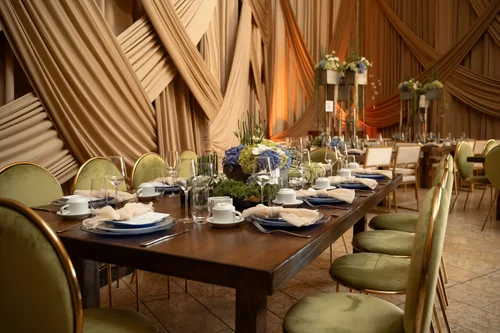 Mesa larga de madera con sillas verdes y drapeados dorados al fondo