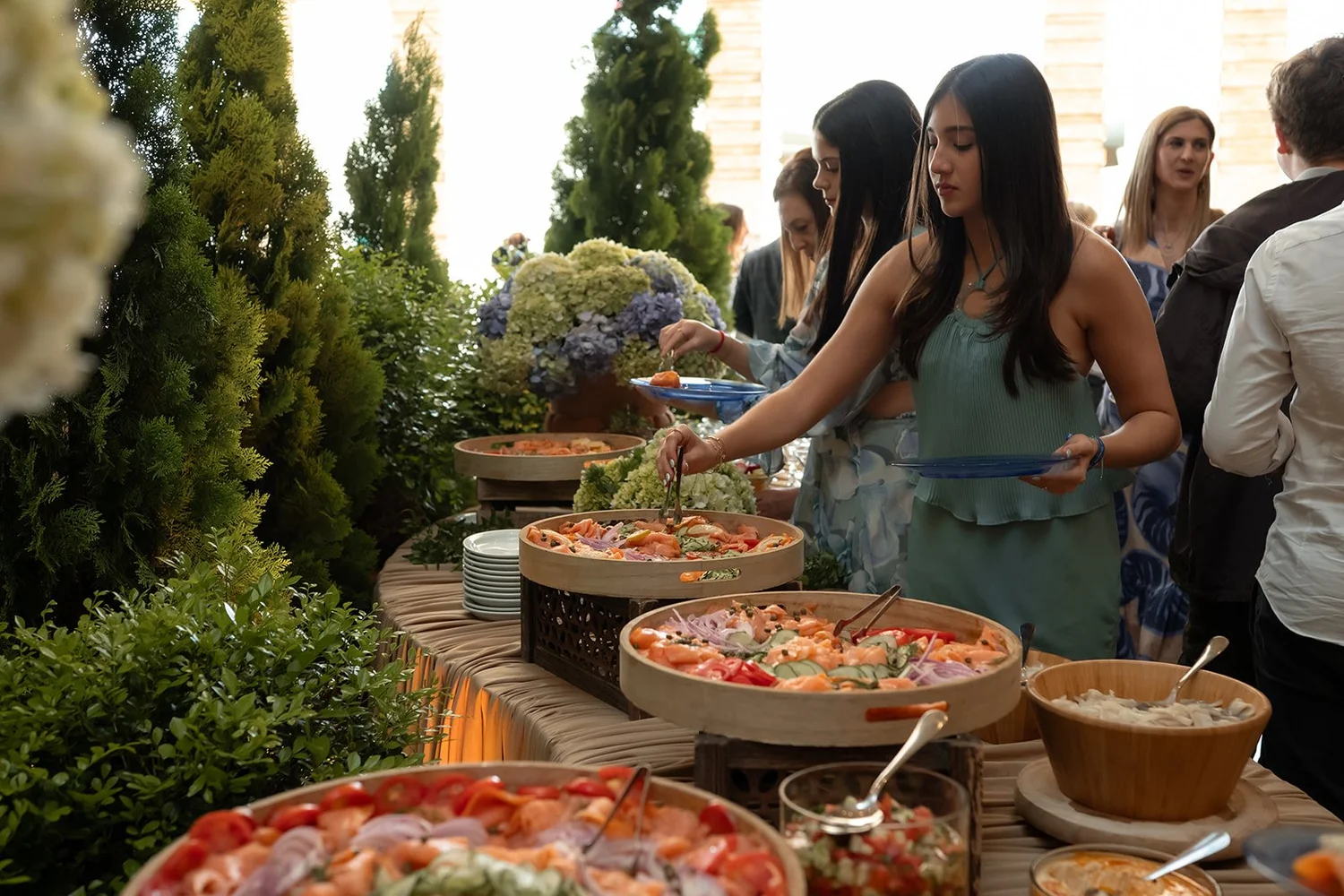 Invitados sirviéndose del buffet junto a las mesas del jardín botánico