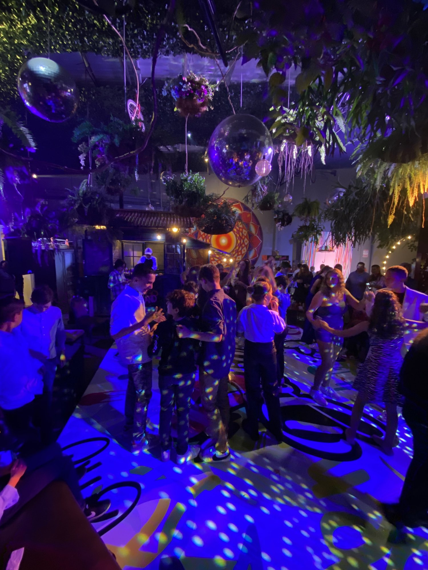 Invitados bailando bajo luces moradas y plantas colgantes