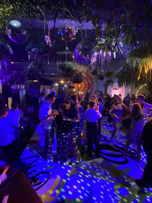 Invitados bailando bajo luces moradas y plantas colgantes