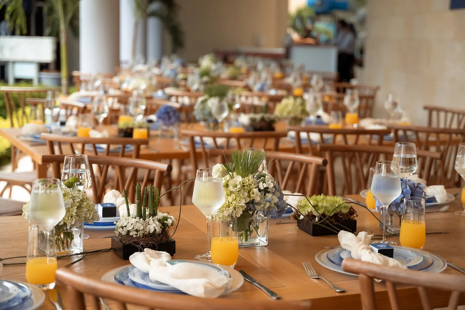 Mesa puesta con vajilla blanca, flores azules y jugos