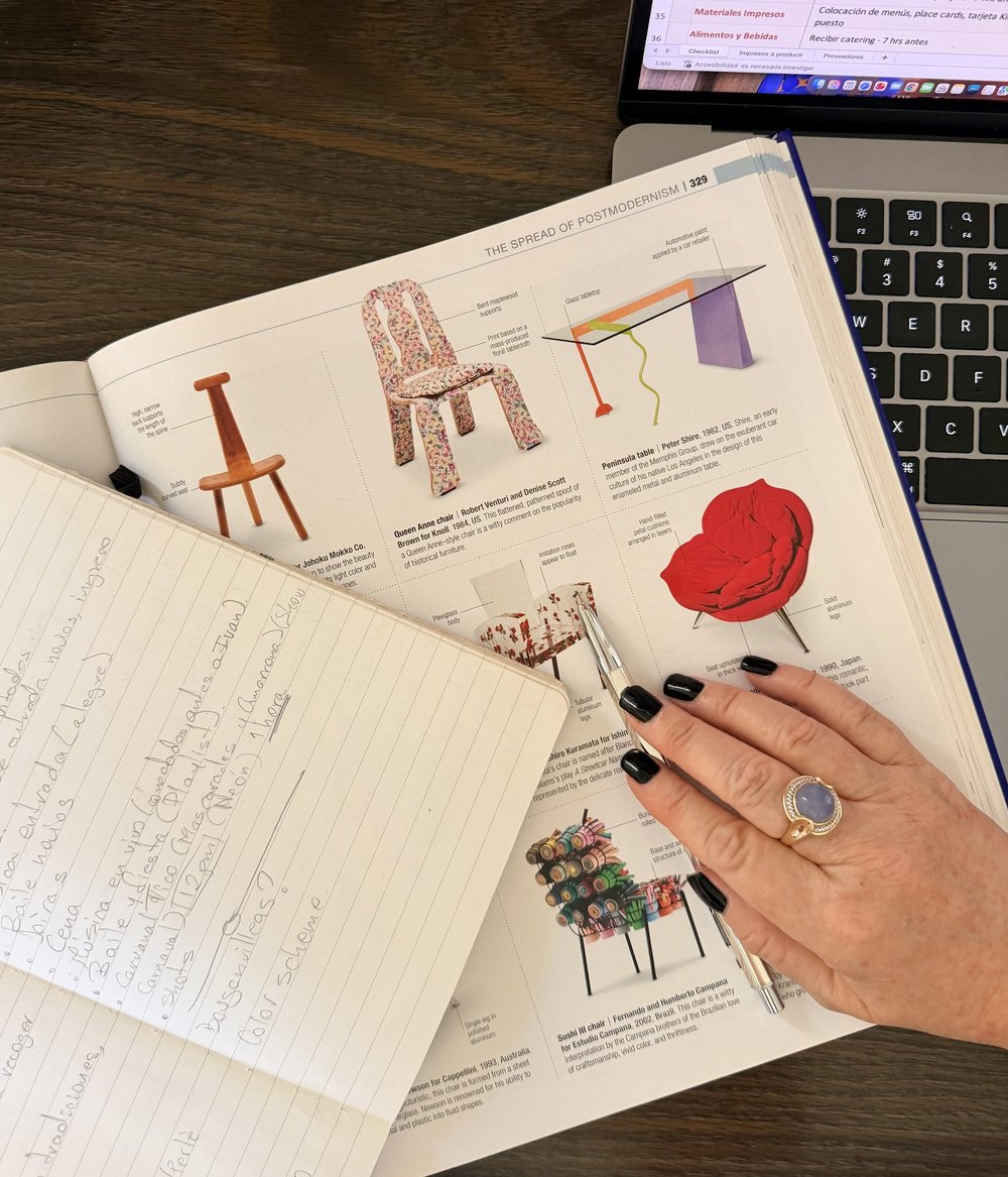 Cuaderno de notas, recortes de diseño de sillas y una laptop sobre el escritorio de Irene
