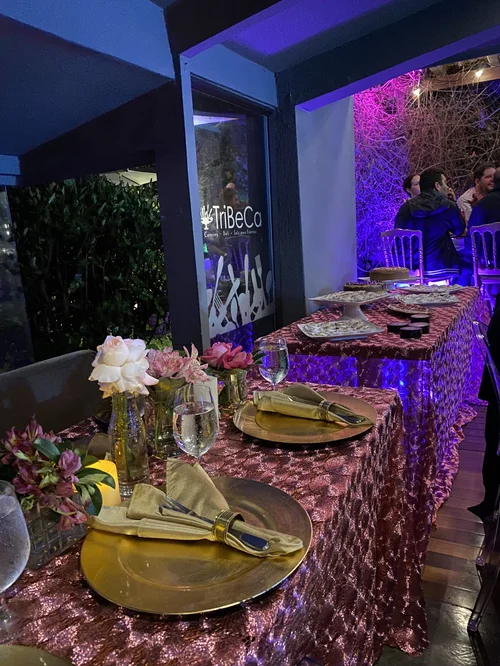 Mesa con mantel de lentejuelas y flores frente a un fondo iluminado en rosa