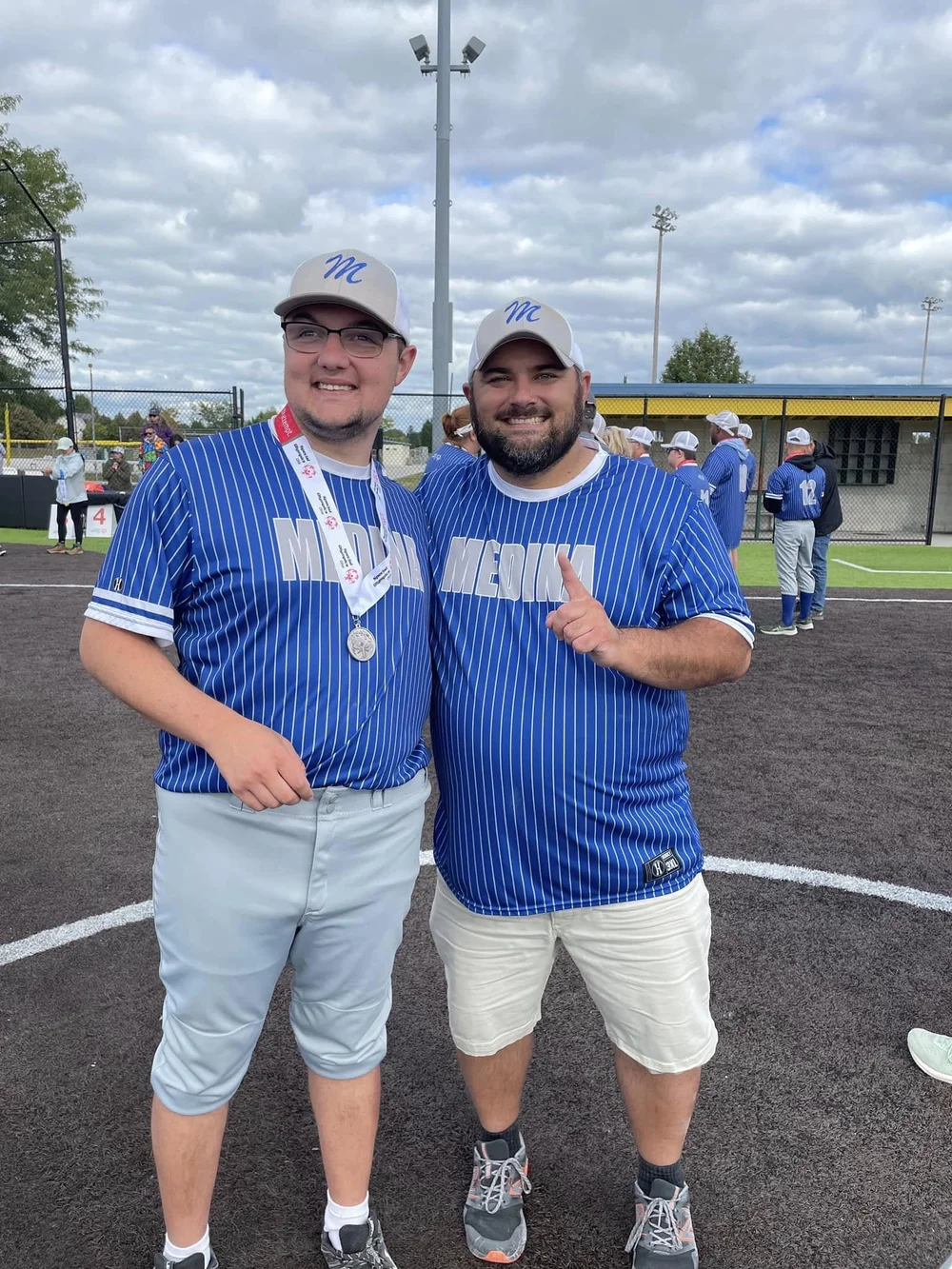 Two Flash softball players in Medina jerseys on the field, one wearing a medal.