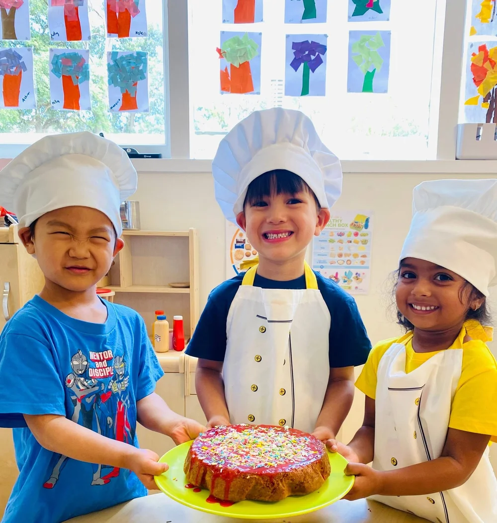 Three Kelvin children dressed as chefs sharing a cake