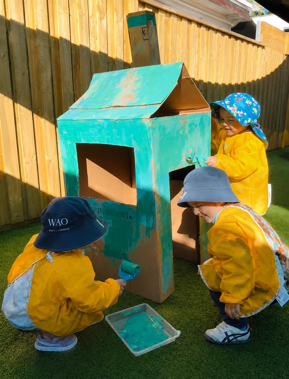 Toddlers exploring a cardboard play house outdoors at Kelvin Kindergarten