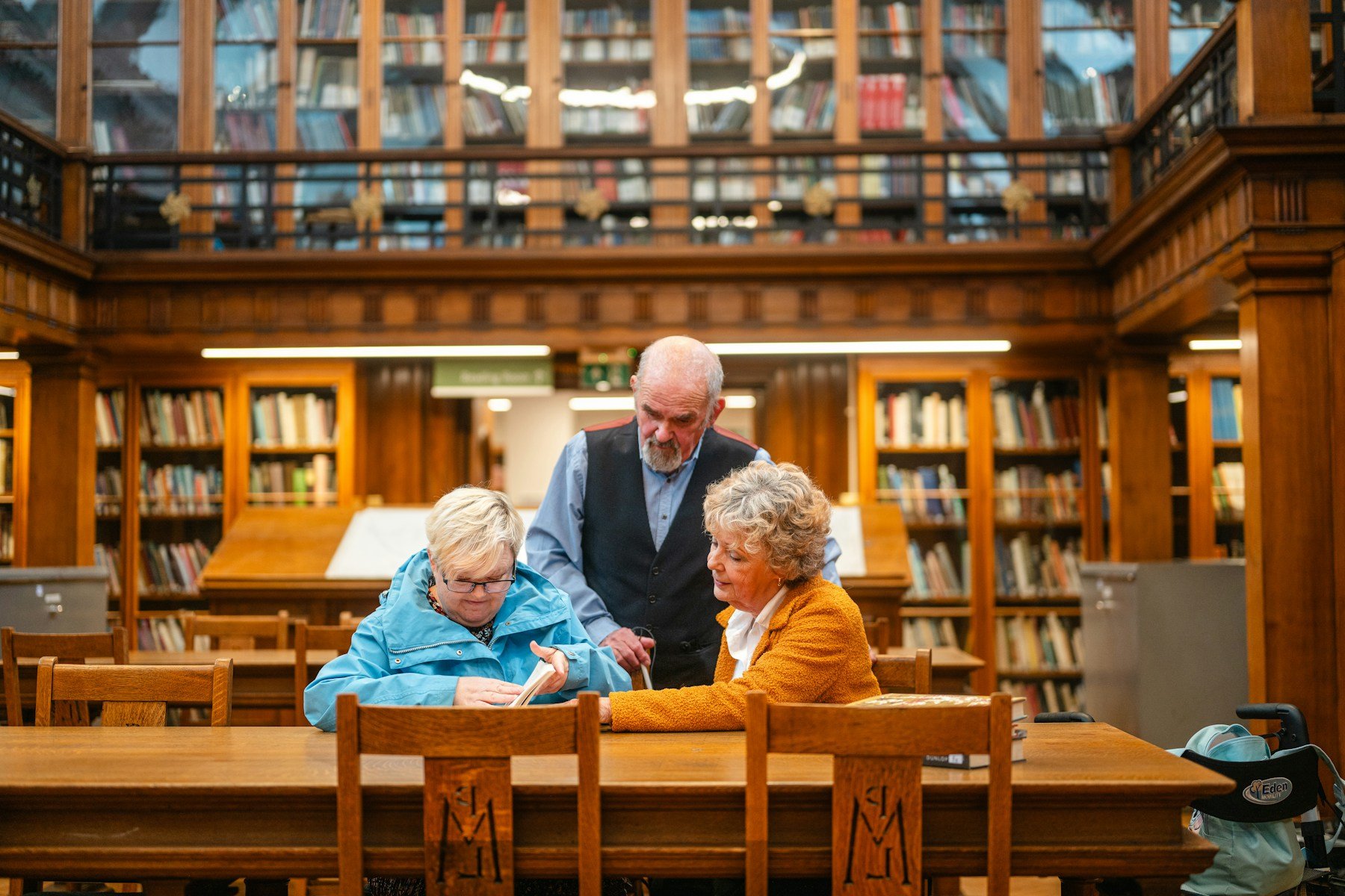 Three adults reading and discussing a book together in a library