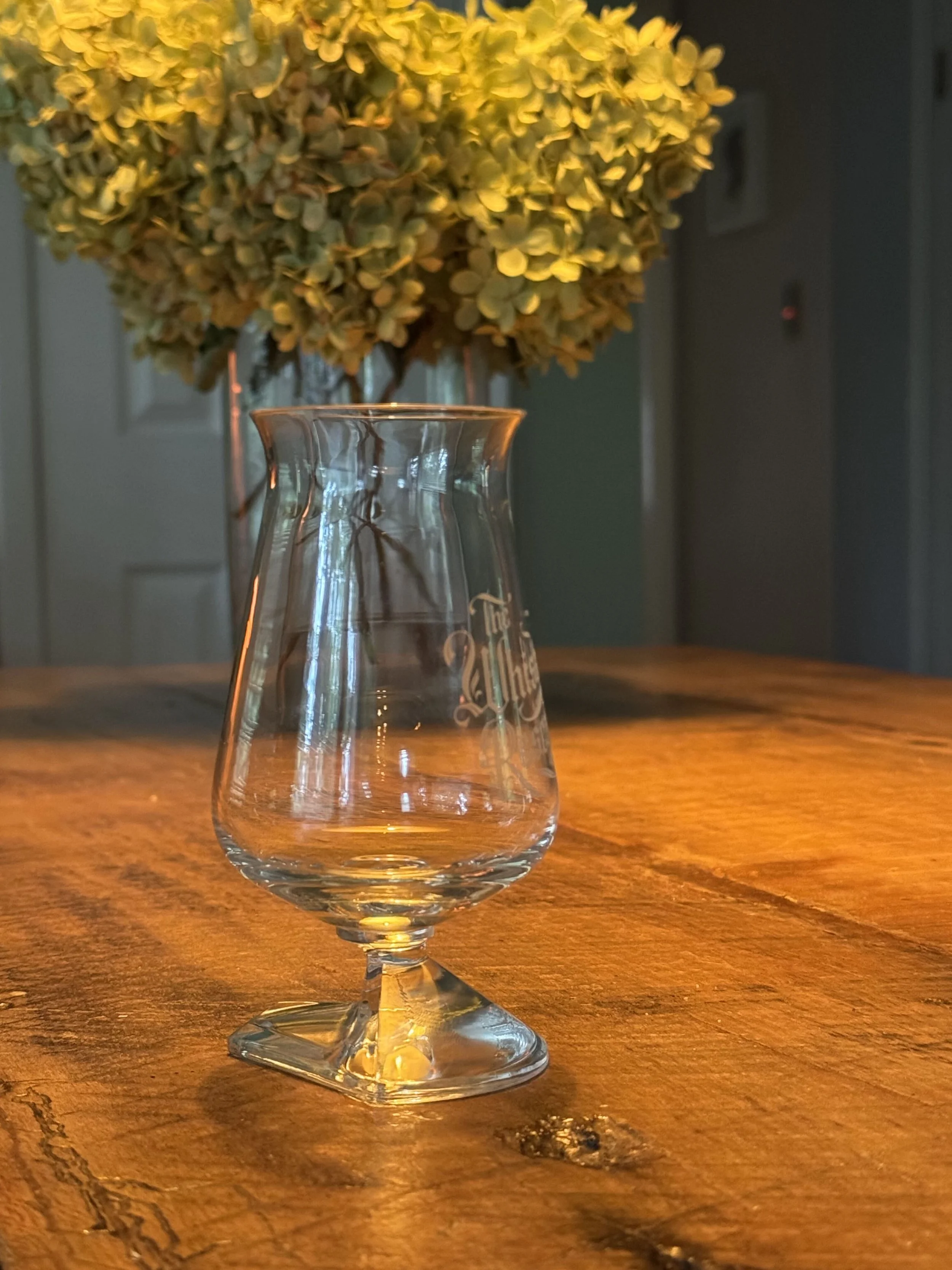 An Irish Whiskey glass that is crystal, with a rock like stem, a deep bowl, a tall glass, and a flared rim