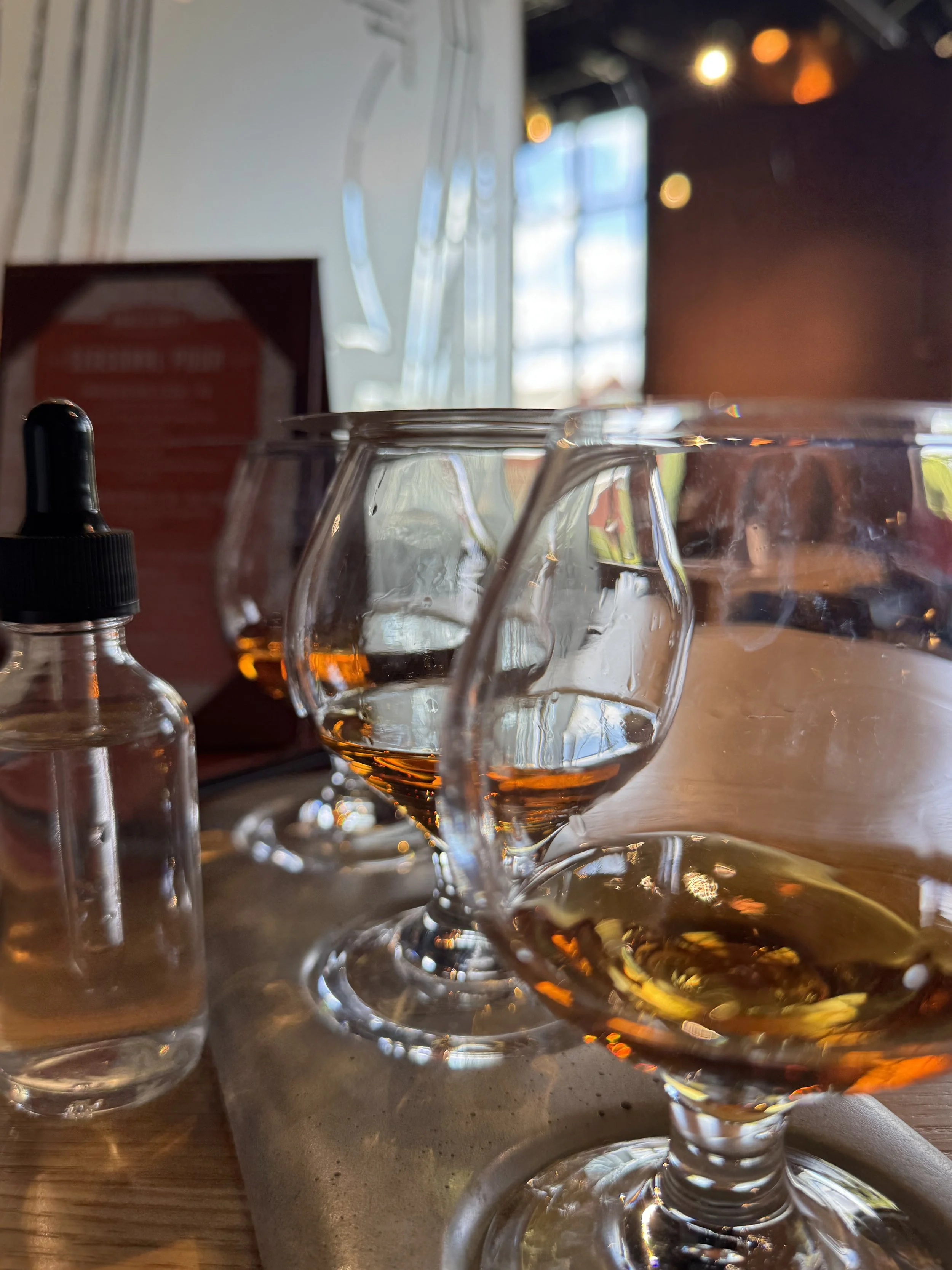 A flight of whiskey with a water dropper on a bar table in a room with a lot of natural light