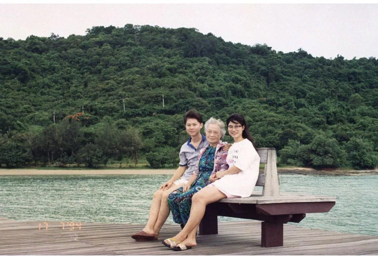 Dr. Rushapol Sdawat sitting on a wooden pier bench by the sea with family, July 1994