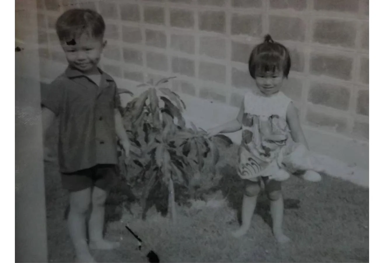 Black-and-white photograph of Dr. Rushapol Sdawat as a small boy, standing in a garden beside a young plant